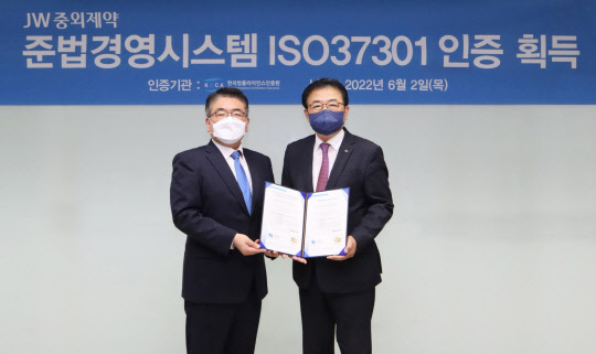 신영섭(오른쪽) JW중외제약 대표이사가 지난 2일 서울 서초동 본사에서 이원기 한국컴플라이언스인증원장에게 ISO37301 인증서를 받은 뒤 기념촬영을 하고 있다. <JW중외제약 제공>